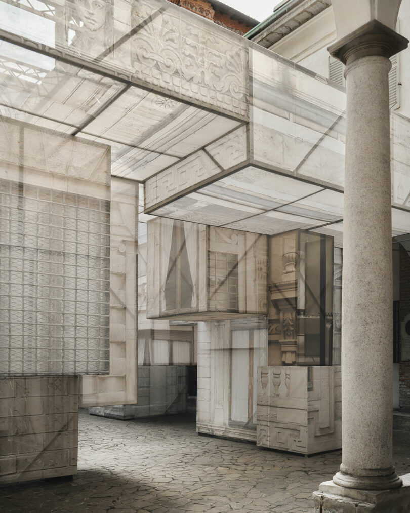 A courtyard with translucent fabric panels printed with architectural designs, suspended around stone columns and above a cobblestone floor.