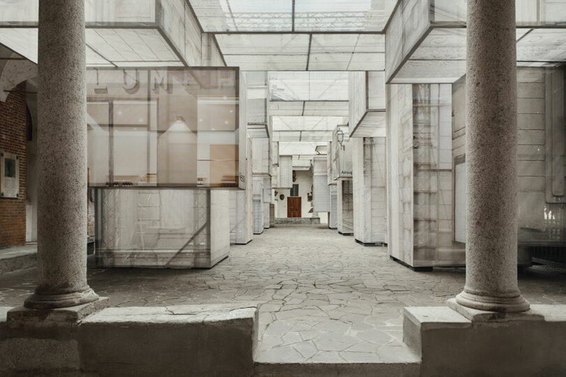 A spacious, modern architectural interior with stone columns, paved floor, translucent panels, and a mix of brick and marble walls.