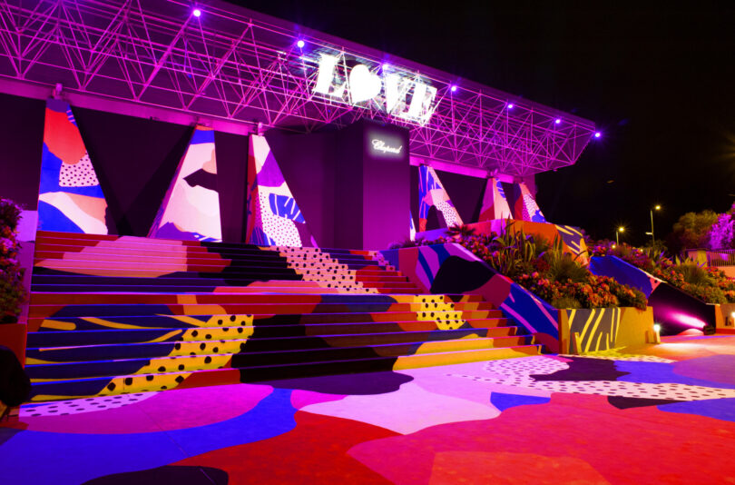 A colorful, geometric-painted staircase and platform are illuminated by purple lights at night, with a glowing "LOVE" sign above the entrance—making it the perfect Friday 5 photo spot.