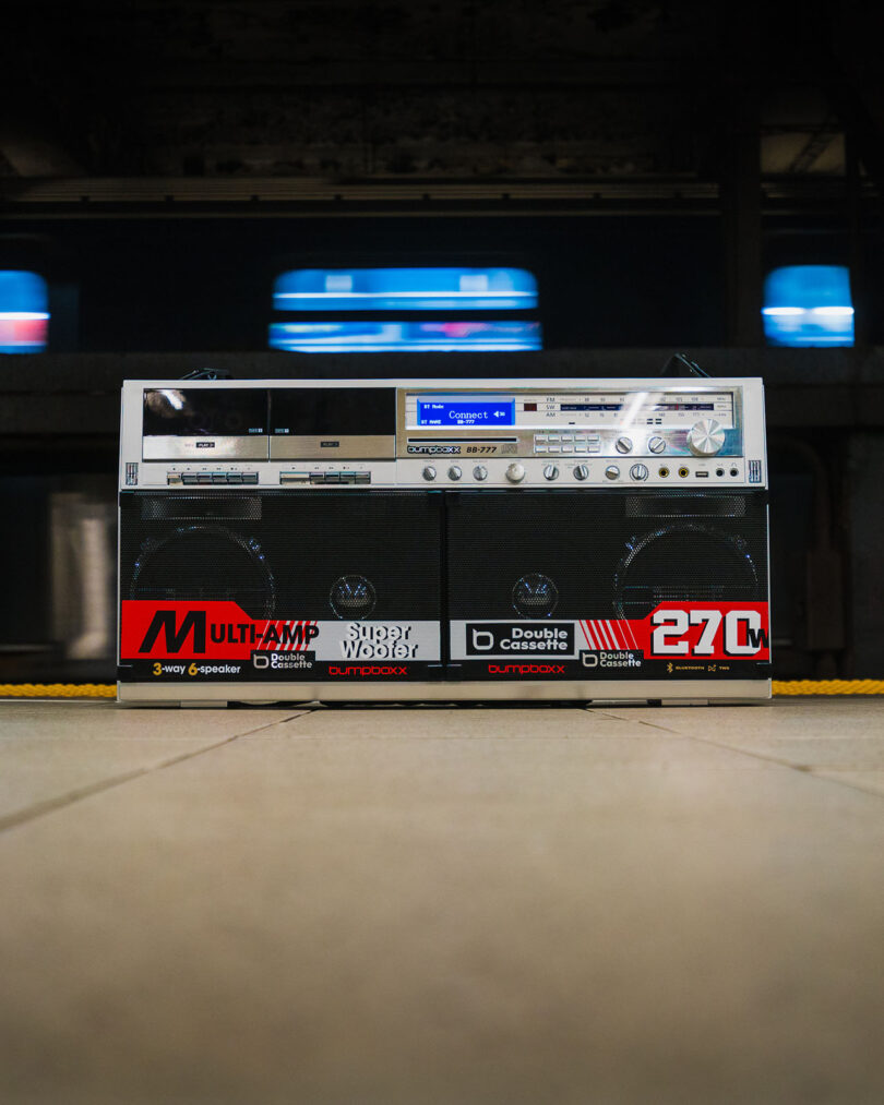 A large retro boombox sits on a subway platform with a moving train blurred in the background.