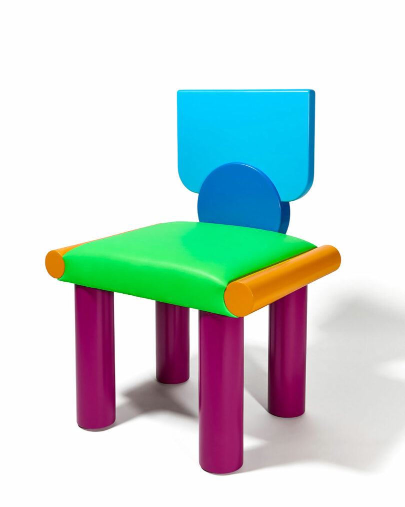 A colorful chair with a blue backrest, green seat, orange armrests, and purple cylindrical legs, set against a white background.