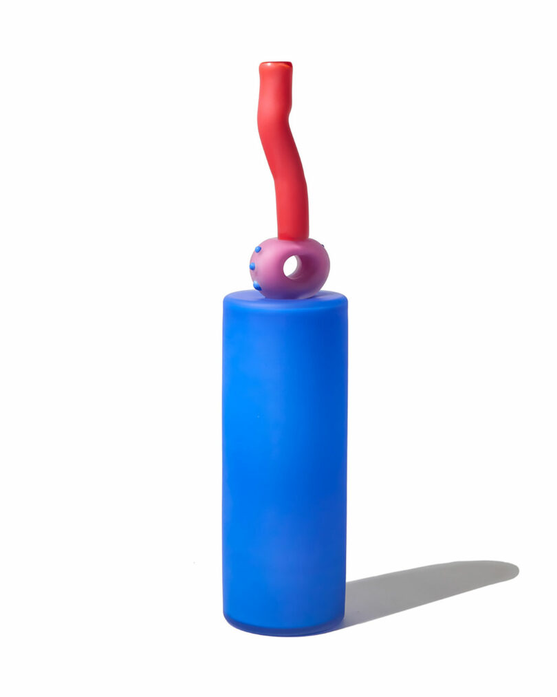A tall cylindrical blue object with a pink, doughnut-shaped ring and a bent red tube on top, inspired by Cedric Mitchell JOOPITER, casting a shadow on a white background.