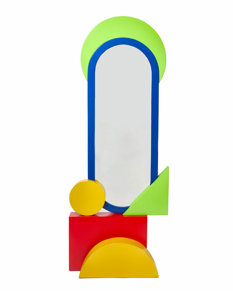 A tall, oval mirror with a blue frame, accented by green, yellow, and red geometric shapes including circles, squares, and triangles.