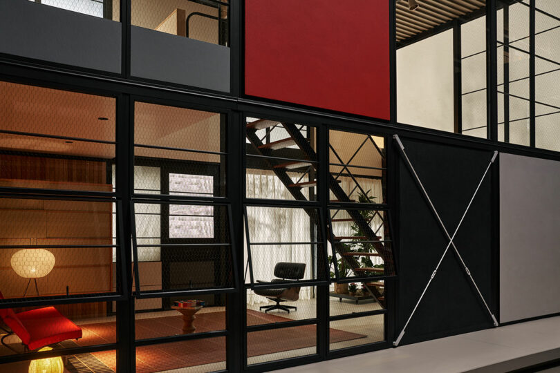 Interior view of a modern building with floor-to-ceiling glass panels, geometric patterns, a staircase, lounge chair, and minimalistic decor.