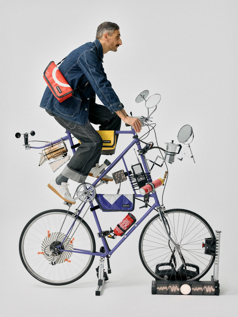 A man rides a stationary bicycle equipped with various gadgets, measuring devices, and mirrors, posed against a plain background.