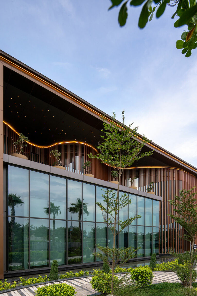 Modern building with large glass windows, vertical wooden slats, and a landscaped garden in the foreground creates a striking confluence of architectural elegance and natural beauty under a partly cloudy sky.