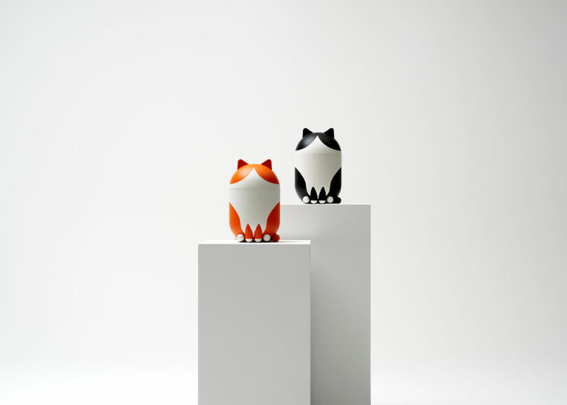 Two geometric, fox-shaped figures—one orange and one black—are displayed on separate white pedestals against a plain white background.