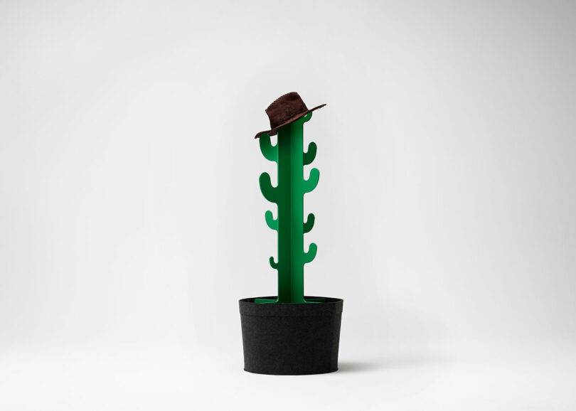 A green, stylized cactus in a black pot with a brown hat placed on top, set against a plain white background.
