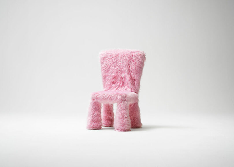 A chair covered in fluffy pink faux fur stands in a white, minimalist setting.