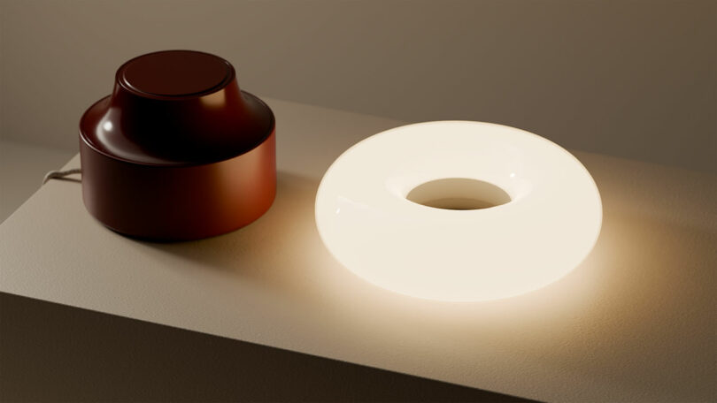A round, glowing white lamp and a brown cylindrical object sit side by side on a light-colored surface.