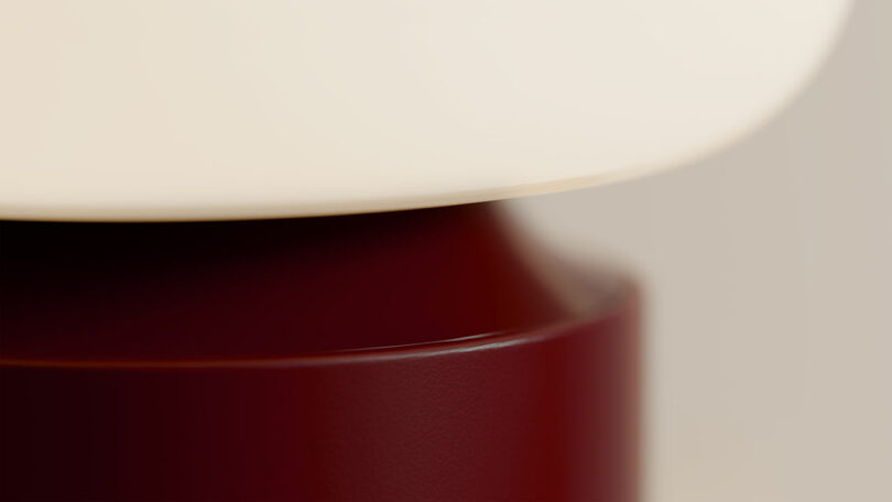 Close-up of a modern lamp with a smooth white shade and a glossy burgundy base.