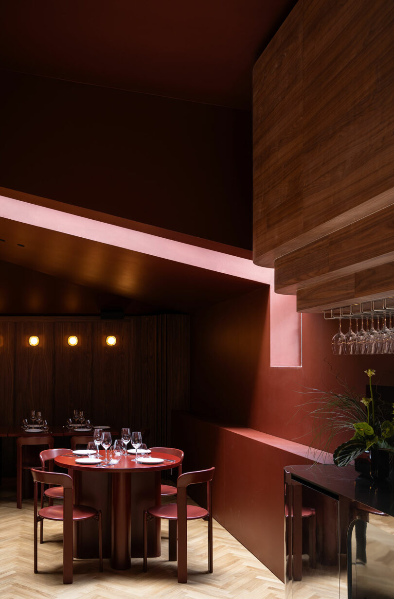 A modern dining area with red walls and ceiling, round red tables, red chairs, wood panel accents, wine glasses, and soft lighting.