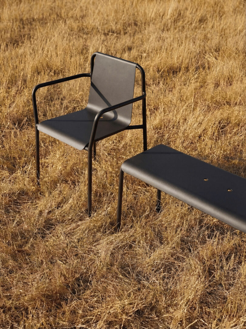 A black metal chair and a matching bench tiptoe across dry, yellow grass in an inviting outdoor setting.