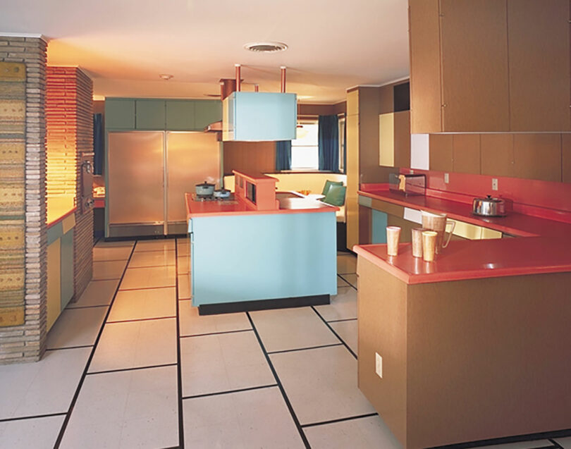 Mid-century modern kitchen with light blue and brown cabinets, red countertops, stainless steel fridge, and geometric black-and-white tile floor.